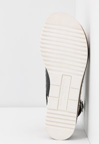 Zwarte geweven leren sandaal met een gestructureerde witte rubberen zool; beschikt over een glad, plat ontwerp en verstelbare hardware voor een goede pasvorm.