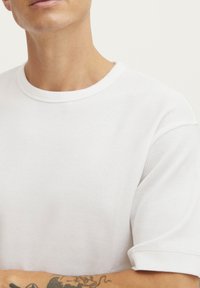 Hvid kortærmet skjorte lavet af struktureret stof, med rund halsudskæring og subtilt vaffelmønster, med opsvømmede ærmer og glat kant.