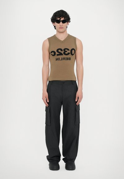 Top marrone senza maniche con il testo nero "032 BERLIN", abbinato a pantaloni cargo neri con tasche laterali e calzature nere chunky.
