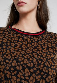 Bruine en zwarte dierenprint trui met een gestructureerd oppervlak, voorzien van een geribbelde halslijn die is geaccentueerd met rood en zwart.