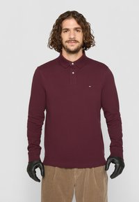 Bordeaux langærmet polo-shirt med krave, tre-knaps placket og lille logo på brystet, sammen med fløjlsbukser.