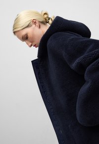 Giacca in fleece blu navy con cappuccio extra-large, caratterizzata da un tessuto testurizzato e dettagli con logo sul davanti. Morbida, vestibilità comoda.