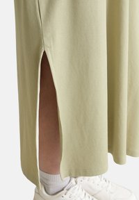 Lichtgroene geribbelde maxi rok met zijsplits, getoond naast witte sneakers en enkelsokken. Gladde textuur, casual ontwerp.
