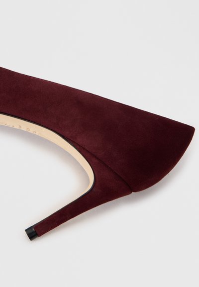 Décolleté in camoscio bordeaux con punta affusolata e design elegante. Presenta un tacco sottile e una punta nera a contrasto sul tallone.