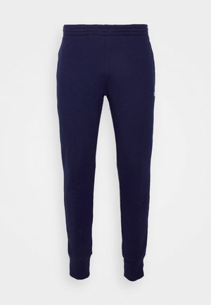 Pantalon de jogging bleu marine fuselé avec taille et poignets élastiques, présentant un petit logo sur la partie supérieure de la cuisse.