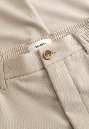 Beige textured fabric trousers with a button closure and a partially visible white label reading "GABBA" inside the waistband.