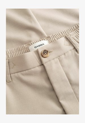 Beige textured fabric trousers with a button closure and a partially visible white label reading "GABBA" inside the waistband.