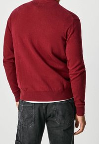 Röd stickad tröja med långa ärmar, ribbade muddar och fåll, samt en slät yta. Buren över svarta cargobyxor.