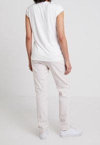 White short-sleeve t-shirt with a round neckline, paired with light beige straight-leg pants and white sneakers; smooth fabric and casual fit.