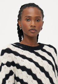 Maglione in maglia con vestibilità ampia, caratterizzato da strisce zigzag alternate in nero e crema. Collo ampio e tessuto texturizzato con punti aperti.