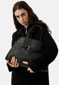 Czarna skórzana torebka o gładkiej fakturze, z konstrukcyjnym designem, górnymi uchwytami i klamrą na przodzie.