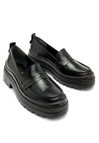Czarne skórzane loafersy na grubej podeszwie, z przeszywanym akcentem na wierzchu stopy i małymi pętelkami na pięcie dla łatwego zakładania.