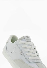 Białe trampki wykonane z materiałów skórzanych i zamszowych. Posiadają siateczkowe wyściółki, białe sznurówki oraz jasnoszare akcenty. Logo znajduje się po boku.