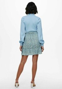 Jersey azul claro acanalado con mangas abullonadas, combinado con una mini falda con volantes y estampado floral en tonos azules y amarillos. Presenta una cintura ajustada.