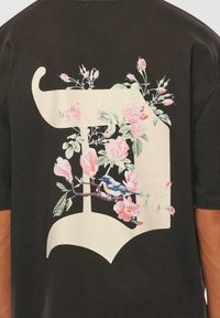 Black short-sleeve t-shirt featuring a large cream and floral graphic with a bird and pink roses on the back.