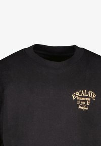 Zwarte katoenen T-shirt met een ronde hals, voorzien van gouden tekst en logo "ESCALATE ESTABLISHED DENIM" aan de voorkant. Zachte textuur, casual ontwerp.