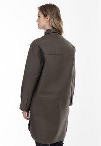 Oliven grøn læderfrakke med lange ærmer, høj krave og lige snit. Har et minimalistisk design og diskrete syninger.