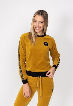 Żółta welurowa bluza z czarnymi akcentami, posiadająca długie rękawy i okrągły dekolt. Logo na piersi i wzorzyste wykończenie na rękawach.