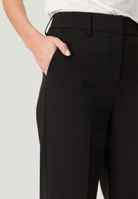 Zwarte broek met een getailleerde pasvorm, met een gladde textuur, zijzakken en een platte tailleband met riemlussen.