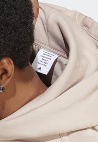 Vaaleanpunainen huppari, jossa on pehmeä kangas ja huppu. Hoito-ohjelapuke näkyvissä, jossa on motivoivia lauseita ja Adidas-logo.