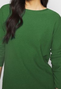 Green knitted sweater featuring a round neckline and long sleeves with cuffed hems. The texture is ribbed and slightly stretchy.
