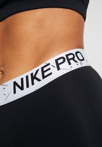 Black athletic leggings featuring a white "NIKE PRO" waistband with a subtle marbled pattern. Smooth texture and fitted design.