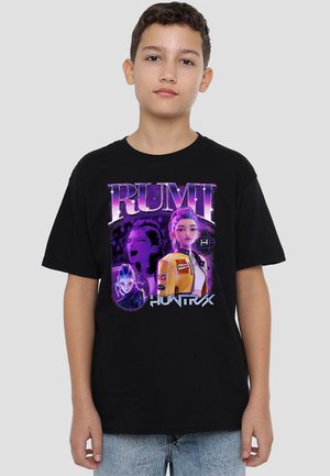 Junge trägt ein schwarzes T-Shirt mit animierten weiblichen Charakteren in Lila und Gelb sowie dem Text "RUMI HUNTRX."