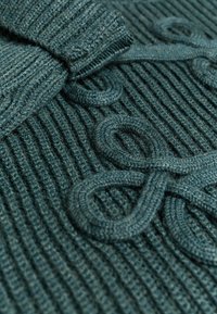 Gebreide trui in donker teal met ribbelstructuur. Bevat gedraaide garenaccenten die in de stof zijn geweven. Zacht materiaal, gemiddelde dikte.