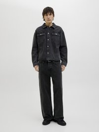 Giubbotto di jeans nero con due tasche frontali, chiusura a bottoni e vestibilità rilassata, abbinato a jeans neri larghi e stivali neri.
