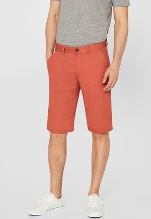 Rode katoenen shorts met een rechte snit, knoopsluiting en twee zijzakken, gecombineerd met witte sneakers en een grijs T-shirt.