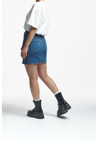 Person walking, wearing a white short-sleeve top, blue denim skirt with back pockets, white socks, and black chunky lace-up boots.