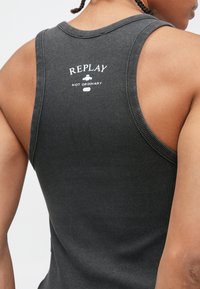 Γκρι ριμπ αμάνικη μπλούζα με στρογγυλή λαιμόκοψη και μεγάλα ανοίγματα στα μανίκια, με λευκό τυπωμένο λογότυπο στην πλάτη.