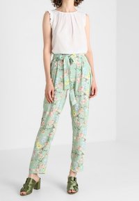 Květinové lehké zelené kalhoty s páskem na zavázání. Spárované s bílým topem bez rukávů a zelenými sandály se zavázáním.