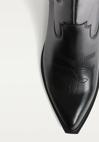 Čierna kožená kovbojská topánka s špicatou špičkou, dekoratívnym prešívaním, vykrojením a hladkým povrchom.