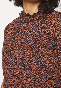 Blåsa i orange och marinblått mönster med rynkad halsringning, texturerat tyg och en lös passform med smockdetaljer.