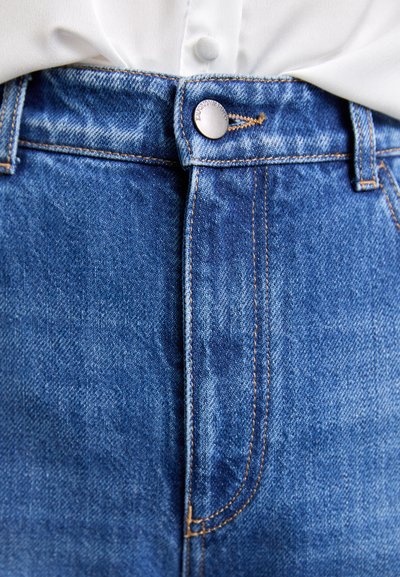 High-waisted blue denim jeans with a zip fly and button closure. Features copper stitching and a subtle wash texture.