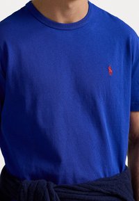 Camiseta de cuello redondo color azul real, confeccionada en algodón, con un bordado del logo de polo rojo en el lado izquierdo del pecho. Textura suave, diseño ajustado.