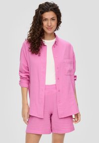 Roze overhemd met knopen en een enkele zak, gecombineerd met bijpassende roze shorts. Gemaakt van zachte, textuurstof. Witte top eronder.