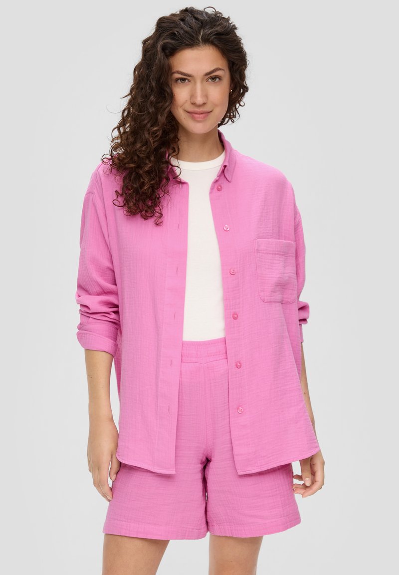 Roze overhemd met knopen en een enkele zak, gecombineerd met bijpassende roze shorts. Gemaakt van zachte, textuurstof. Witte top eronder.