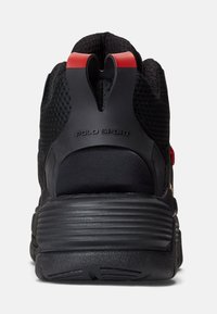 Černá sportovní bota s texturovaným síťovým svrškem, červeným akcentem na patě a zvýšeným poutkem. Disponuje silnou, drsnou podrážkou pro podporu.