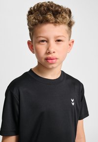 T-shirt noir à manches courtes en tissu lisse avec un col rond et un petit logo en chevron blanc sur la poitrine gauche.