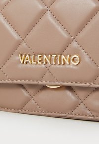 Κρεμ ζακάρ δερμάτινη τσάντα Valentino με χρυσά λογότυπα κα�ι λεπτομέρειες ραφής στο κλείσιμο της πασχαλίνης.