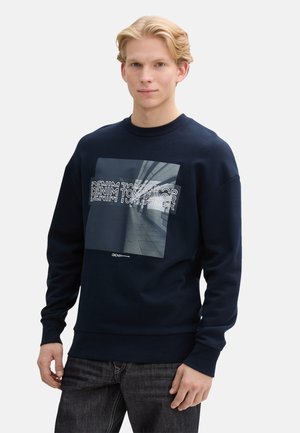 Sudadera azul marino de mezcla de algodón con un estampado gráfico en la parte delantera. Presenta puños y dobladillo de canalé, con un ajuste en general relajado.
