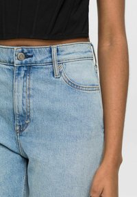 Jean en denim bleu clair avec une taille mi-haute, des poches avant et un léger effet usé. Fini avec un bouton en métal et des coutures contrastantes.