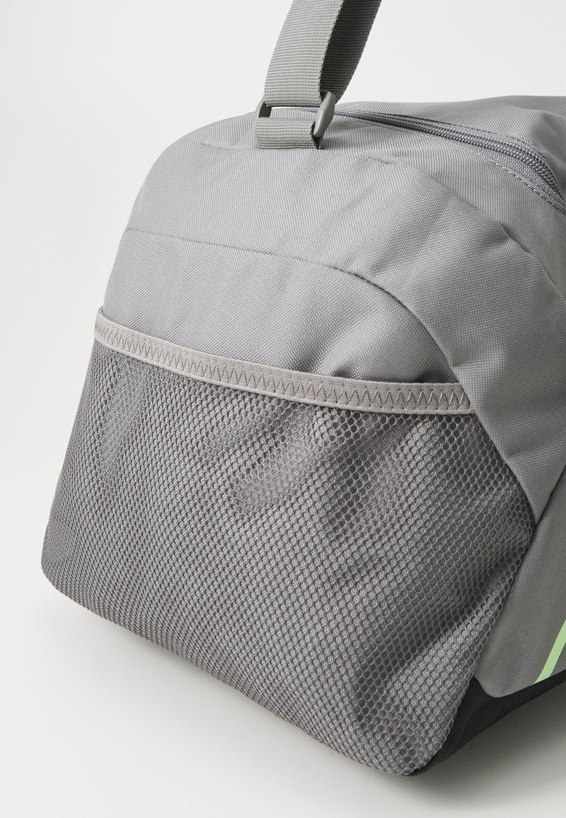 Sac en tissu gris avec une poche en maille texturée, fermeture éclair et une sangle robuste. Présente des accents vifs et une forme structurée.