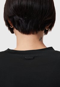 Svart kortärmad skjorta med rund halsringning. Har en minimalistisk etikett nära halsen och ett slätt, texturerat tyg.