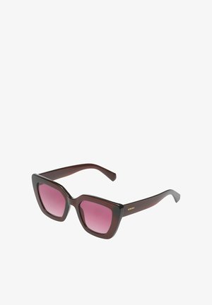 Donkerbruine oversized cat-eye zonnebril met roze verloopglazen en "KOMONO"-logo op het montuur, schuin gezien op een witte achtergrond.