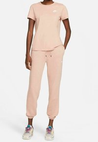 Ljusrosa Nike-t-shirt och matchande leggings, tillverkade av mjukt, texturerat tyg. Vitt logotyp på t-shirten och byxorna, med dragsnörning.