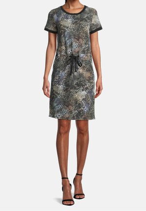 Kvinde iført en knælængde, kortærmet kjole med slangeprint og sort kant, samt sort bælte i taljen, kombineret med sorte hæle med ankelrem.