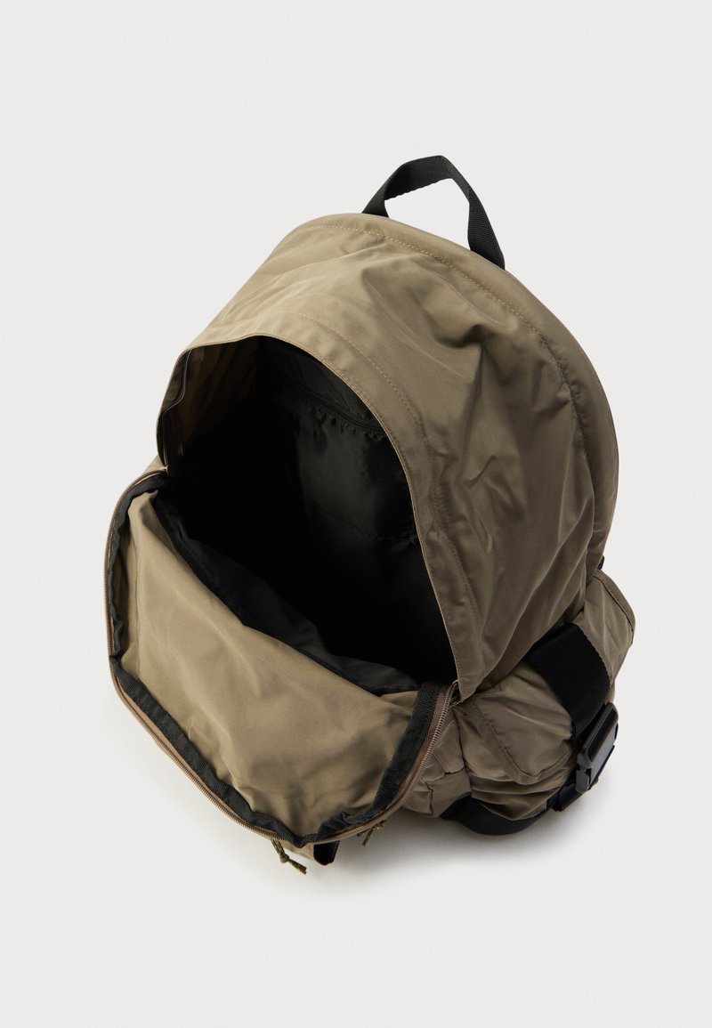 Khaki backpack with a soft, textured exterior. Features a zippered main compartment and a black interior. Finished with adjustable straps.